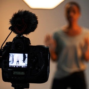 A camera records a young woman, who is acting in the background