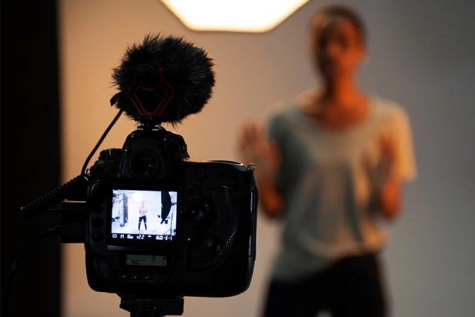 A camera records a young woman, who is acting in the background