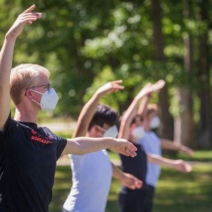 Masked dancers rehearse on a tennis court