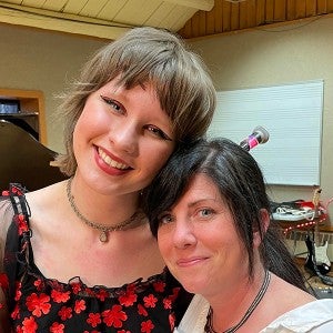 A student in a black and red top stands smiling with her arm around her smiling teacher, who is wearing a white shirt.