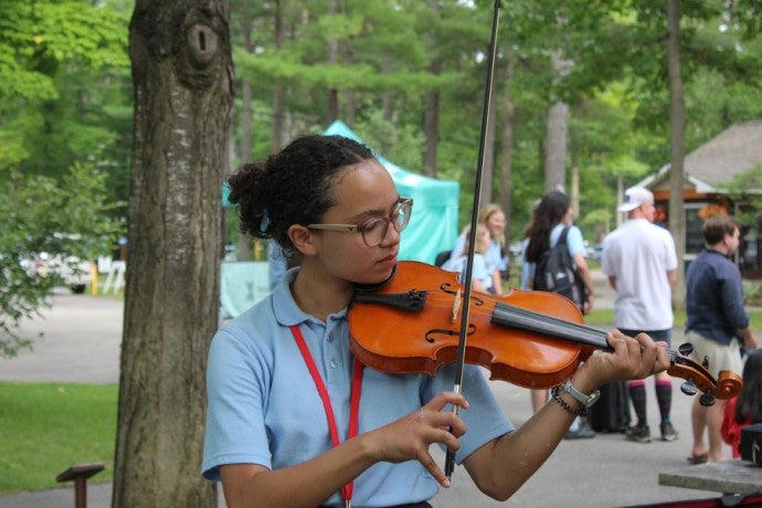 A young student plays a violin outdoors.