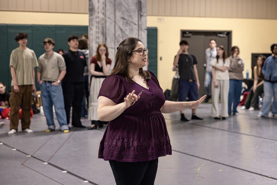 A woman dressed in purple speaks to a group of students.