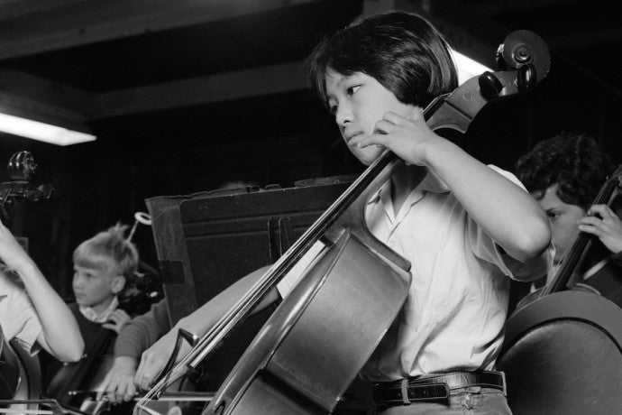 A child with short hair and wearing a light-colored shirt is deeply engaged in playing the as part of a children's orchestra. 