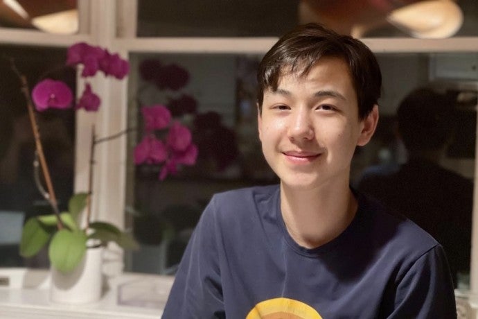 A student with short hair and dark eyes smiles into the camera near a pot of orchids.