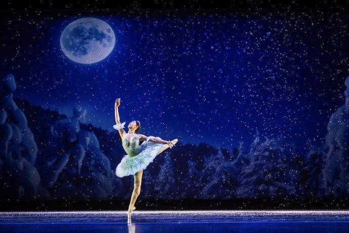 A dancer moves gracefully in front of a wintry scene.