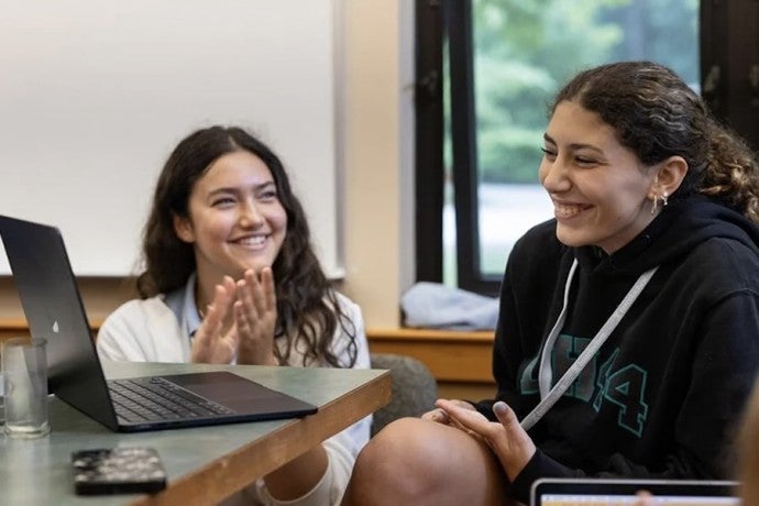 Two students laugh and clap during a writing workshop.