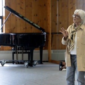 An elderly woman, stylishly dressed, teaches a class of dance students.