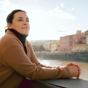 A woman dressed in a camel coat stares pensively from her perch on a bridge.