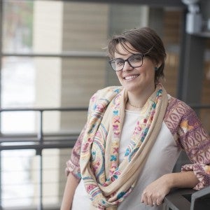 A woman with short brown hair and glasses smiles at the viewer.