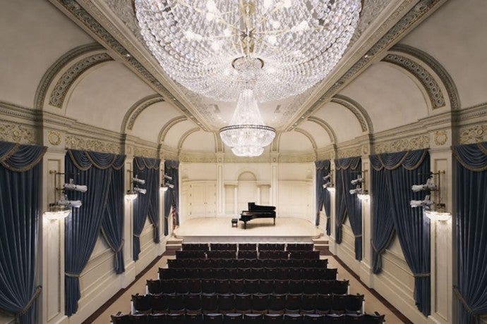 Shot of a stunning, chandelier-hung recital hall with a piano onstage.