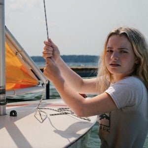 An actor holds a line on a sailboat on a sunny day.