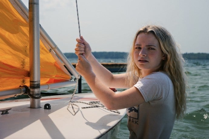 An actor holds a line on a sailboat on a sunny day.
