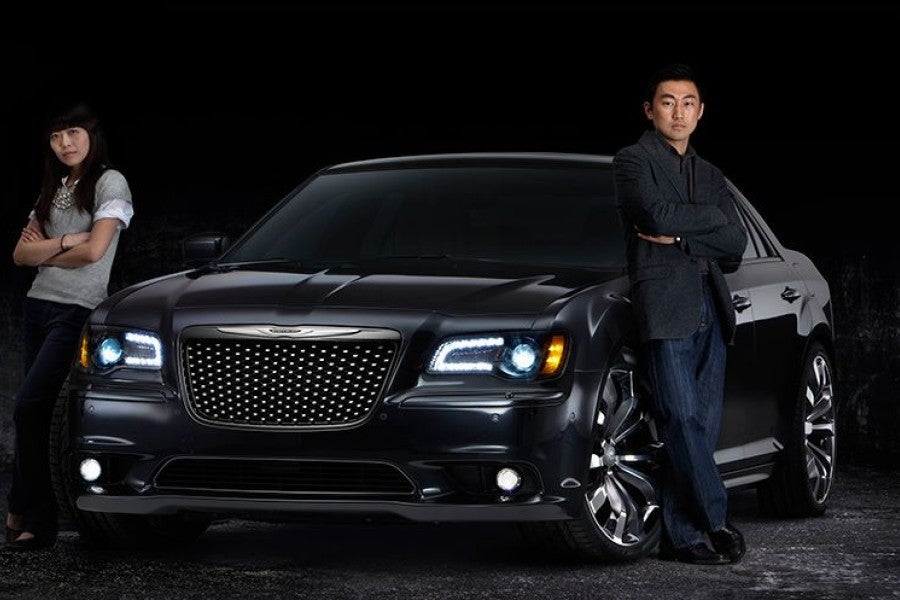 A man and woman stand next to a black car